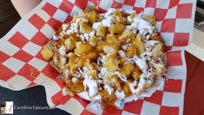 Chicken & Waffle Funnel Cake - juicy pieces of fried chicken atop a golden, sweet funnel cake finished off with a special mandarin orange sauce and powdered sugar. Crossroads Funnel Cakes