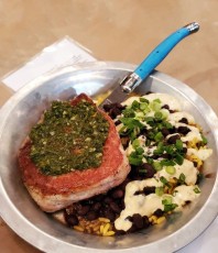 Churrasco Pork Ribeye: tequila brined & grilled center cut pork ribeye, topped with citrus-herb chimmichuri, served with turmeric yellow rice & cuban style black beans topped with house-made chipotle ranchero, and scallons.